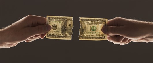 Hands holding torn one hundred dollar bill. Photo : Mike Kemp