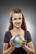 Portrait of girl (12-13) holding globe and looking at camera, studio shot. Photo : FBP
