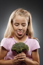 Girl (8-9) holding broccoli and sticking out tongue, studio shot. Photo : FBP