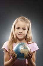 Portrait of girl (8-9) holding globe and looking at camera, studio shot. Photo : FBP