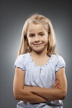 Portrait of girl (8-9) looking at camera with arms crossed, studio shot. Photo : FBP