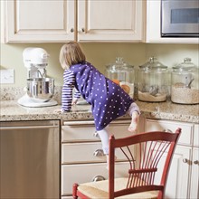 USA, Utah, Girl (2-3) climbing on cupboard in kitchen. Photo : Tim Pannell
