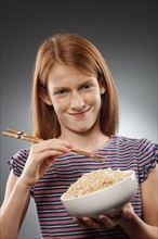 Portrait of redhead girl (10-11) holding chopsticks and bowl of rice, studio shot. Photo : FBP