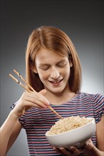 Portrait of redhead girl (10-11) holding chopsticks and bowl of rice, studio shot. Photo : FBP