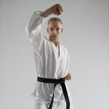 Young man performing karate stance on white background.