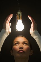 Woman looking up at illuminated lightbulb.