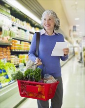 USA, New Jersey, Jersey City, Senior woman carrying shopping basket in supermarket.