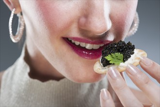 Young woman eating caviar on biscuit.