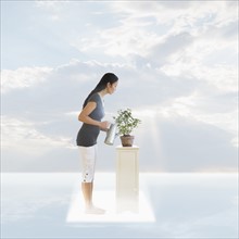 Woman watering plant under cloudy sky.