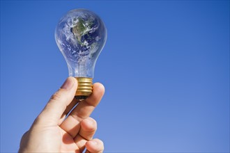 Hand holding lightbulb with globe. Photo : Daniel Grill