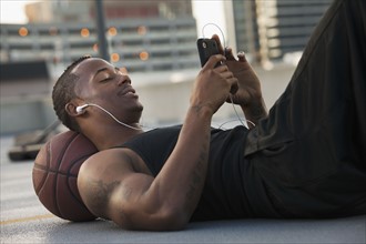 USA, Utah, Salt Lake City, Young man lying on basketball and listening to mp3 player. Photo : Mike