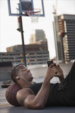 USA, Utah, Salt Lake City, Young man lying on basketball and listening to mp3 player. Photo : Mike