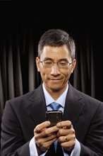 USA, Utah, Provo, Smiling businessman standing in front of black curtain and text messaging. Photo