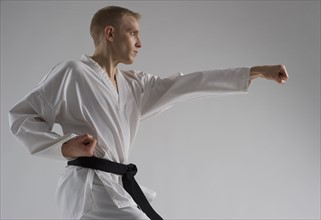 Young man performing karate stance on white background.