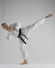 Young man performing karate kick on white background.