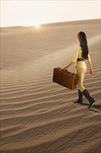 USA, California, Death Valley, Woman with suitcase walking in desert.