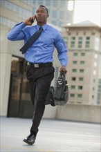 USA, Utah, Salt Lake City, Young businessman running and talking on mobile phone. Photo : Mike Kemp