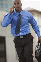 USA, Utah, Salt Lake City, Young businessman running and talking on mobile phone. Photo : Mike Kemp