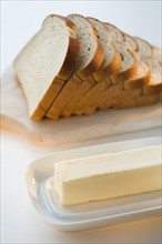 Sliced bread on chopping board beside butter.