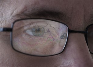 Close-up of man's eye with graph reflecting in glasses. Photo : Daniel Grill