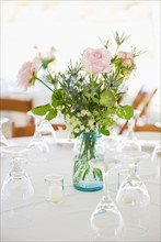 Vase of roses on set dinner table with glasses.