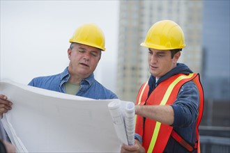 USA, New Jersey, Jersey City, Construction workers studying blueprints on construction site.