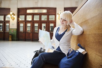 USA, Seattle, Young woman sitting at train station and reading map. Photo : Take A Pix Media
