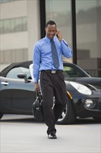 USA, Utah, Salt Lake City, Young businessman walking and talking on mobile phone. Photo : Mike Kemp
