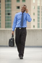 USA, Utah, Salt Lake City, Young businessman walking and talking on mobile phone. Photo : Mike Kemp