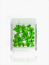Studio shot of green thumbtacks in glass cube. Photo : David Arky