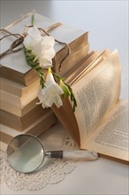 Magnifying glass beside stack of books with flowers.