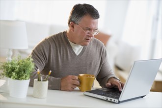 USA, New Jersey, Jersey City, Man using laptop, holding drink in living room.