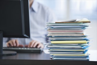 USA, New Jersey, Jersey City, Paperwork on desk by businessman using computer.