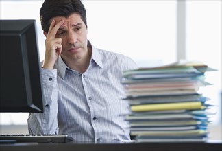 USA, New Jersey, Jersey City, Businessman staring at stacked paperwork on desk.