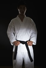 Portrait of young man performing karate stance on black background.