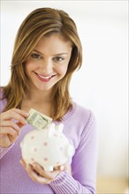 USA, New Jersey, Jersey City, Portrait of young woman putting banknote to piggybank.
