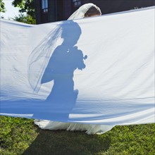 Silhouette of bride behind large sheet in garden.