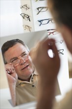 USA, New Jersey, Jersey City, Man trying on glasses in shop mirror.