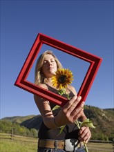 USA, Colorado, Young woman holding picture frame and sunflower. Photo : John Kelly