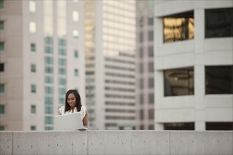 USA, Utah, Salt Lake City, Young businesswoman using laptop in front of skyscrapers. Photo : Mike