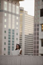 USA, Utah, Salt Lake City, Young businesswoman using laptop in front of skyscrapers. Photo : Mike