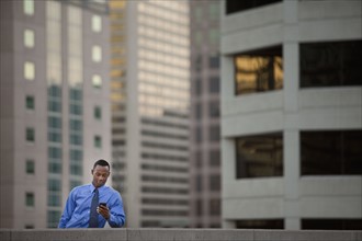 USA, Utah, Salt Lake City, Young businessman text messaging in front of skyscrapers. Photo : Mike