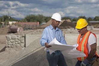 Two construction workers discussing blueprints on building site. Photo : Dan Bannister