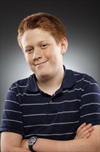 Portrait of redhead teenage boy (14-15) with arms crossed, studio shot. Photo : FBP