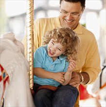 USA, California, Los Angeles, Father with son (4-5) sitting on carousel's horse. Photo : FBP