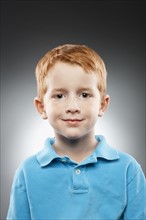 Portrait of smiling redhead boy (4-5) wearing blue polo shirt, studio shot. Photo : FBP