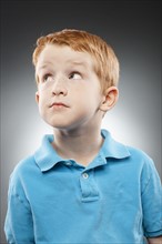 Portrait of smiling redhead boy (4-5) wearing blue polo shirt and looking up, studio shot. Photo :