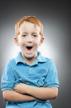 Portrait of smiling redhead boy (4-5) wearing blue polo shirt and making face, studio shot. Photo :