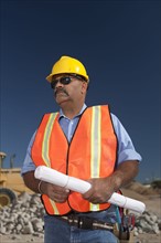 Construction worker holding blueprint on building site. Photo : Dan Bannister