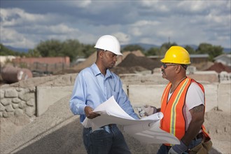 Two construction workers discussing blueprints on building site. Photo : Dan Bannister